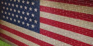 A man in a suit standing in front of a large American flag painted on a wall