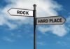 Directional signpost with ROCK and HARD PLACE labels against a blue sky