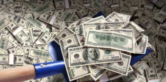 A shovel filled with stacks of cash on a background of scattered dollar bills