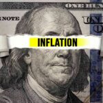 A torn paper strip with the word 'INFLATION' over a hundred dollar bill featuring Benjamin Franklin