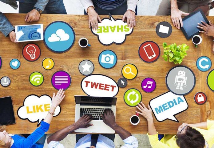 Top view of a collaborative workspace with social media icons and people using laptops