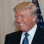 A smiling man in formal attire with an American flag in the background