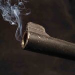 Close-up of a gun barrel emitting smoke against a black background