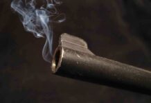 Eight Kids SHOT–Public PARK Under Fire Close-up of a gun barrel emitting smoke against a black background