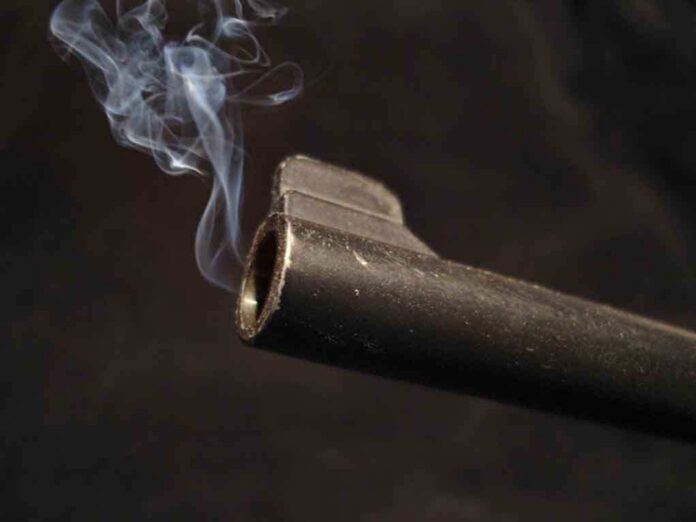 Close-up of a gun barrel emitting smoke against a black background
