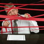A man tangled in red tape while trying to sign a contract