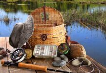Fishing gear including a hat, basket, and fishing rods arranged by a serene water body