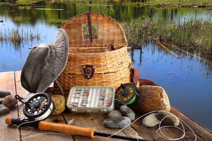 Fishing gear including a hat, basket, and fishing rods arranged by a serene water body