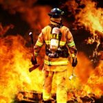Firefighter standing in front of a large fire, equipped with tools
