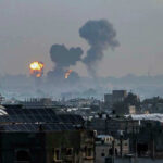 Iran Strikes LNG Giant, Qatar Burns Flames and smoke billowing over a cityscape.