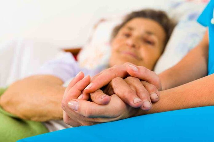 shutterstock_161459273.jpg A caregiver holding the hands of an elderly patient in a hospital bed