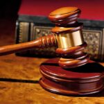 A wooden gavel resting on a polished surface with a law book in the background