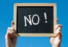 A hand holding a chalkboard with the word NO written on it against a blue sky