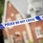 Police tape reading POLICE DO NOT CROSS in front of a house