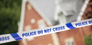 Police tape reading POLICE DO NOT CROSS in front of a house