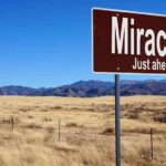 A road sign reading 'Miracles Just ahead' in a desert landscape