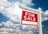 A red For Sale sign against a blue sky with clouds