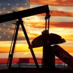 Silhouette of an oil pump jack against a sunset background with an American flag overlay