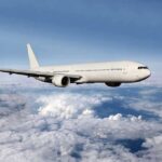Birth on Plane Reveals ABSURD Citizenship Gamble A white airplane flying above fluffy clouds in a blue sky