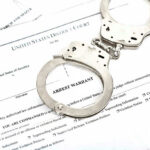 Iranian Arms Scandal Explodes in U.S. Handcuffs on top of an arrest warrant document.
