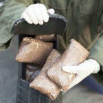 Person handling packages wearing gloves and green jacket.