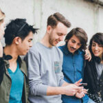 Phone Addiction’s Shocking Impact On Birth Rates Group of friends looking at a smartphone.