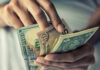 Dollar Crisis Looms: Will It Collapse? Person holding multiple U.S. dollar bills.