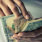 Dollar Crisis Looms: Will It Collapse? Person holding multiple U.S. dollar bills.