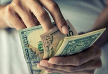 Dollar Crisis Looms: Will It Collapse? Person holding multiple U.S. dollar bills.