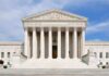 Judge SLAMS Trump Admin’s $100M Grant Cut Front view of the Supreme Court building with large columns and steps under a blue sky