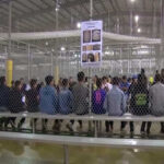 DOJ-DHS Crackdown: Who ‘Lost’ These Kids? People sitting on benches inside a fenced facility.