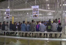 People sitting on benches inside a fenced facility.