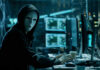The Most Dangerous AI Attack Could Soon Hit America Person wearing mask and hoodie at computer desk.