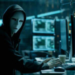 The Most Dangerous AI Attack Could Soon Hit America Person wearing mask and hoodie at computer desk.