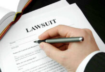 Hand holding pen, filling out lawsuit form.