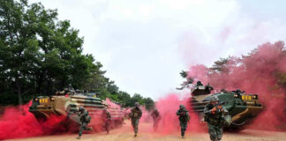 Soldiers running from armored vehicles with red smoke.