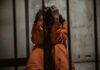 Idaho’s Firing Squad: Quick Death Or Torture? Person in orange jumpsuit sitting behind bars, handcuffed.