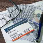 Medicaid Fraud Factories Exposed Medicare card glasses pen money on wooden table