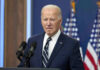 Man in suit speaking at podium with American flags.