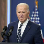 Hearing MELTDOWN Over One Simple Question Man in suit speaking at podium with American flags.