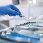 Fake Dentist Vanishes — FBI On Alert Gloved hand holding a dental mirror over instrument tray