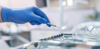 Gloved hand holding a dental mirror over instrument tray