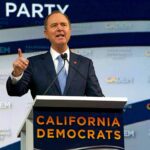 Blue MAGA Bombshell Shocks Democrats Man in suit speaking at a podium with microphones