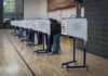 Election Lies Mint Millions — The Game Exposed Voters at polling booths in a gymnasium