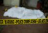 crime scene tape in foreground with covered body in background