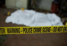 Body Found At ‘Squad’ Tied Property crime scene tape in foreground with covered body in background
