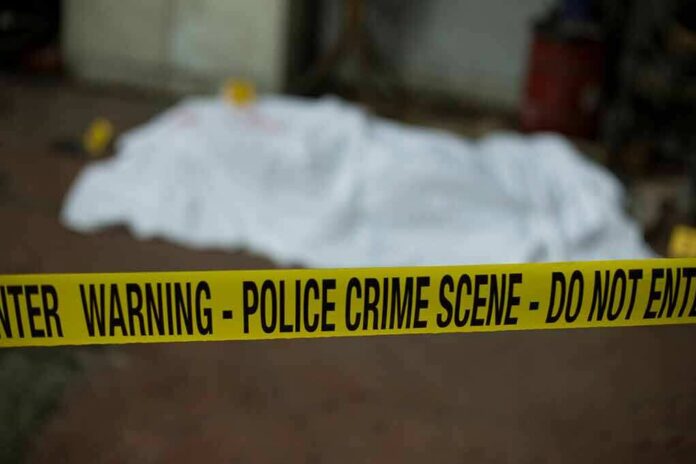shutterstock_788116414 crime scene tape in foreground with covered body in background