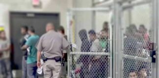 Detention facility with people behind chain-link fence and officer nearby