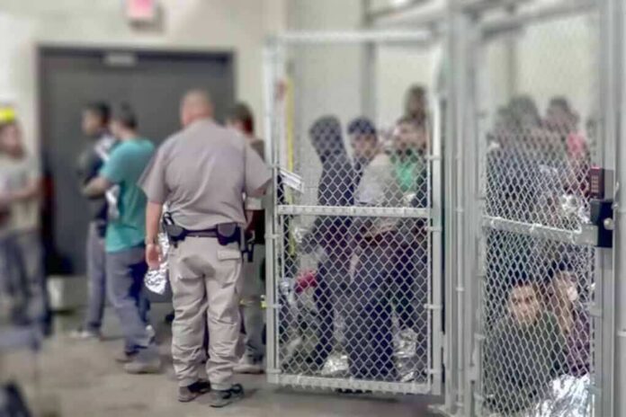 shutterstock_1229072188-1 Detention facility with people behind chain-link fence and officer nearby