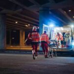 Trauma Warnings Ignored — Girl Jumps Paramedics load a stretcher into an ambulance at night under an overpass